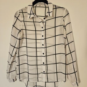 Vit rutig skjorta - Vit skjorta från Outfitters Nation i storlek XS med svart rutigt mönster. Skjortan har klassisk krage, svarta knappar framtill och på ärmsluten samt lång ärm. Tunt och lätt material.