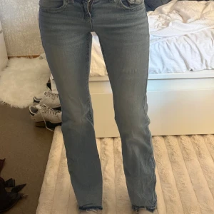 Ljusblå jeans från Gina Tricot - Säljer ett par ljusblå jeans från Gina Tricot med raka ben och snygga detaljerade bakfickor med lock och knapp. Jeansen har klassisk femficksdesign och är tillverkade i mjukt denimtyg. Perfekta för en avslappnad och trendig look.