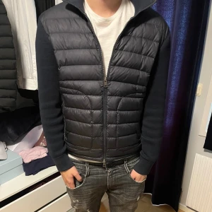 Moncler cardigan  - Snygg mörkblå cardigan från Moncler med quiltad framsida och stickade ärmar och rygg. Jackan har dragkedja framtill, hög krage och Moncler-logga på ärmen. Perfekt för dig som vill ha en stilren och modern look. Finns dock en liten defekt att necktagen saknas 