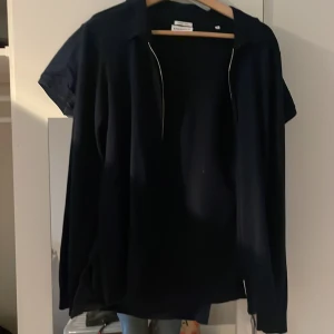 Mörkblå merinoullskofta från Lindbergh - Snygg mörkblå kofta från Lindbergh i merinoull med slim fit-passform. Koftan har dragkedja framtill, klassisk krage och långa ärmar. Perfekt för dig som vill ha en stilren och bekväm look året runt.