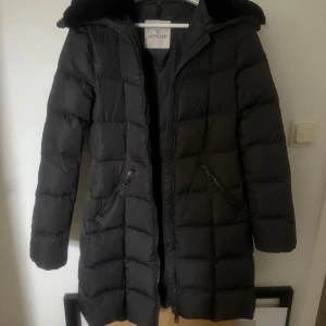 Moncler jacka  - Säljer denna långa varma Moncler jacka, perfekt nu till vintern/hösten. Använd fåtal gånger, inga täcken på användning. Inga fläckar eller slitningar någon stans!! Självklart äkta-se bild med qr koden. Mörkgrå med fårskinn runt kragen som är avtagbart med ett annat lager under så man kan välja. Storlek S. Snabb affär prioriteras. Hör av dig vid frågor eller funderingar😊