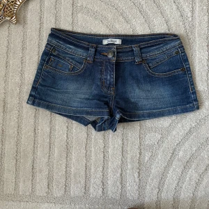 Mörkblå jeansshorts från Denim Life - Snygga mörkblå jeansshorts från Denim Life med klassisk femficksdesign, slitna detaljer och kontrastsömmar. Shortsen har låg midja, bälteshällor och coola bakfickor med broderad detalj. Perfekta för varma dagar och en avslappnad look.