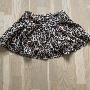 Leopardmönstrad kortkjol från Gina Tricot - Snygg kortkjol från Gina Tricot med leopardmönster i beige, brunt och svart. Kjolen har en bred resår i midjan och är lätt utställd för en cool och avslappnad look. Perfekt för dig som vill sticka ut med ett djurmönster.💕