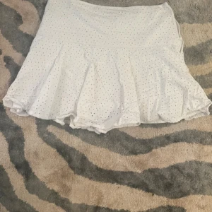 Vit volangkjol från H&M i bomull - Supersöt vit kortkjol från H&M i bomull med broderade hål och volangkant. Kjolen har en feminin passform och stängs med dragkedja i sidan. Perfekt för en fräsch och somrig look! (Högst upp på dragkedjan har ”hooken” gått sönder, man dragkedjan fungerar som vanligt)