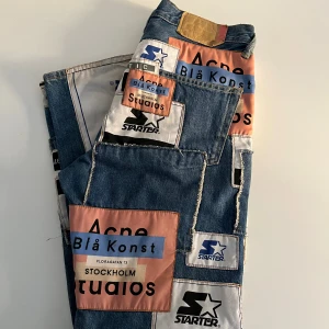 Acne Studios Blå Konst patchade jeans - Unika blå jeans från Acne Studios Blå Konst i samarbete med Starter, med stora patchar i rosa, blått och vitt. Jeansen har raka ben, mid midja och  kontrastsömmar. Strl 27/31. Mindre slitage längs med vid anklarna, se bild.