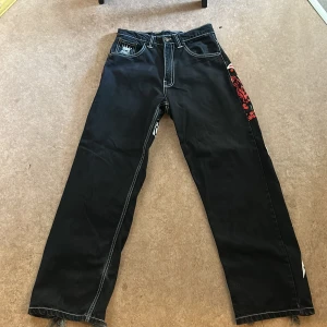 Svarta Bsat jeans med tryck W30 L32 - Unika svarta jeans från Bsat med stora vita och röda tryck på baksidan och slitna benslut. Snygga kontrastsömmar och detaljer som sticker ut. Perfekta för dig som vill ha ett statement-plagg i garderoben.