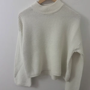 Vit ribbad stickad tröja med hög krage - Säljer en vit stickad tröja med ribbad struktur och hög krage. Tröjan har lång ärm och en relaxed, lite boxig passform. Perfekt för lager-på-lager och enkel att styla till olika outfits.