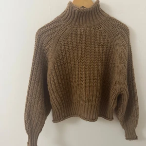 Brun stickad polotröja - Säljer en chunky brun stickad polotröja med hög krage och breda ribbade muddar. Tröjan har en loose fit och långa ärmar, perfekt för kyliga dagar. Den grova stickningen ger en cool och avslappnad vibe.