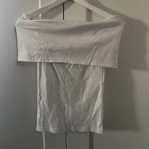 Vit offshoulder tubtopp - Säljer en stilren vit tubtopp med offshoulder-design. Toppen har en bred kant upptill och är kritvit i färgen!