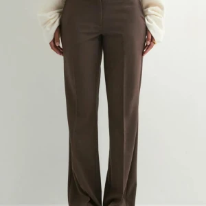 Bruna kostymbyxor med wide fit - Snygga bruna kostymbyxor med raka, vida ben och klassisk passform. Byxorna har lågmidja och pressveck framtill för en clean look. Perfekta att styla med en oversized tröja eller skjorta för en trendig vibe. Nypris 399:-