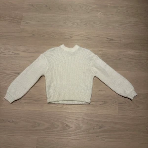 Vit stickad tröja med rund hals - En enkel och stilren vit stickad tröja med rund halsringning och långa ärmar. Tröjan har ribbade muddar vid ärmslut och nederkant, vilket ger en klassisk och mysig look. Perfekt för lager-på-lager under kyliga dagar.