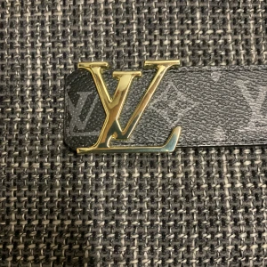 Louis Vuitton svart monogram skärp - Svart Louis Vuitton skärp i skinn med klassiskt monogrammönster och stor LV-logga i guldmetall som spänne. Bältet har exklusiv känsla och tydliga detaljer, perfekt för dig som vill sticka ut med en ikonisk accessoar.