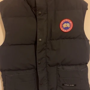 Svart dunväst från Canada Goose - Svart dunväst från Canada Goose med klassisk logga på bröstet. Storlek S men passar även M 