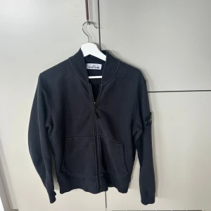 Svart ziptröja från Stone Island - Svart ziptröja från Stone Island med klassisk logga på ärmen. Tröjan har dragkedja framtill, två fickor och ribbade muddar. Köpte den på flagship i London och den gick för ungefär 4000kr. 