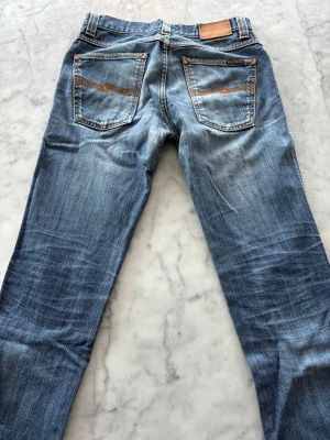 Blå nudie jeans, 31/32 - Ska sälja mina nudiejeans då de har blivit för små för mig. Modellen heter Slim Jim och den tillverkas inte längre. Dry Broken Twill, 100% Bomull. Slitna men inga hål. Skriv om ni har några fler frågor :)
