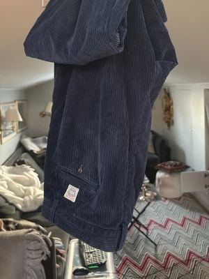 Mörkblå Ralph Lauren manchesterbyxor  - Säljer ett par mörkblå manchesterbyxor med breda ribbor och en liten patch vid bakfickan. 