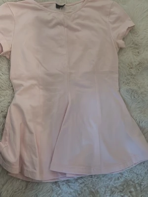 Ljusrosa blus från Gina Tricot - Supersöt ljusrosa blus från Gina Tricot i storlek XS. Toppen har korta ärmar, rund halsringning och lätt utsvängd nederdel som ger en feminin siluett. Perfekt att styla med jeans eller kjol för en fräsch look.