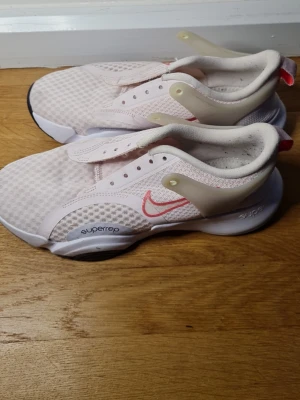 Nike Superrep ljusrosa sneakers - Nike Superrep sneakers i ljusrosa mesh med vita och transparenta detaljer samt rosa Swoosh. Skorna har en chunky vit sula och ventilerande ovandel i syntetmaterial. Perfekta för träning och har en modern, sportig look.