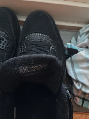 Svarta Nike Air Jordan 4 sneakers - Säljer ett par helsvarta Nike Air Jordan 4 sneakers med klassisk mesh och mockadetaljer. Skorna har snörning, ikoniska Jumpman-loggor på plösen och hälen samt en chunky sula. Perfekta för dig som vill ha en clean och tidlös look.