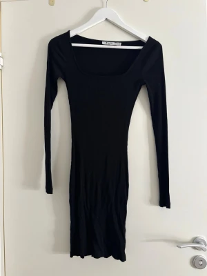 Svart ribbad klänning från NA-KD - Säljer en svart, ribbad klänning från NA-KD i storlek XS. Klänningen har lång ärm, fyrkantig ringning och är figurnära med kort längd. Perfekt för dig som gillar en enkel men snygg look.
