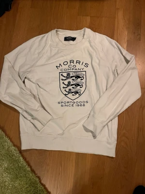 Vit Morris tröja   - Säljer en vit tröja från Morris  med svart tryck framtill och klassiskt lejonemblem. Tröjan är i 100% bomull och har rund hals. Den är lite uttvättad. Priset går att diskuteras