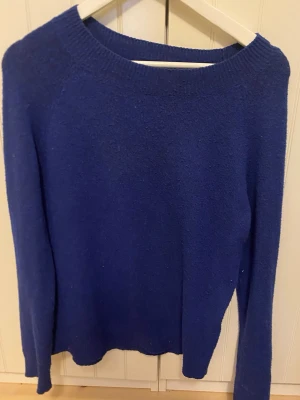 Blå stickad tröja med rund hals - Mysig blå stickad tröja med rund halsringning och långa ärmar. Perfekt för kyliga dagar och enkel att matcha med jeans eller kjol. Tröjan har en klassisk passform och ribbade muddar vid halsen.