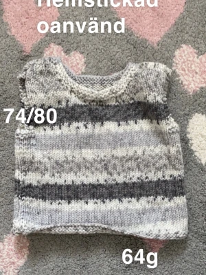 Randig stickad väst i grå toner - Handstickad väst i mjukt garn med randigt mönster i olika grå och vita nyanser. Perfekt att dra över en långärmad tröja för extra värme. Passar storlek 74/80. 🌸 Oanvänd.hemstickad. Ca storlek 74/80