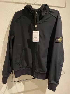 Svart vindjacka från Stone Island - Säljer min sons Stone Island windbreaker i storlek L men passar även dig som har M. Jackan är köpt och äkthetsgranskad av Vestiaire Collective. 