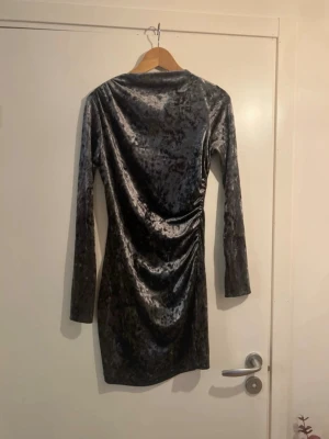 Grå sammetsklänning från H&M - Supersnygg grå sammetsklänning från H&M i kort modell. Klänningen har lång ärm, figurnära passform och snygg rynkning på sidan som ger en cool effekt. Tillverkad i mjuk polyester med lite stretch för extra komfort.