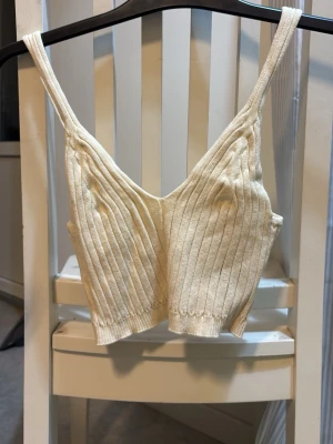 Ribbad beige Linne  - Säljer en ribbad linnetopp i beige stickat material. Toppen har smala axelband, v-ringning och croppad passform. Aldrig använd, väldigt stretchig i materialet