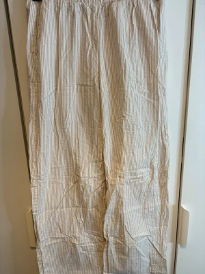 Randiga linnebyxor från Kappahl XS - Säljer ett par ljusbeige och vita linnebyxor från Kappahl i storlek XS. Byxorna har smala vertikala ränder, elastisk midja och är tillverkade i ett lätt och luftigt linnematerial. Perfekta för chill dagar och sommarhäng.