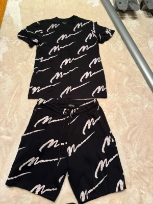 Svart t-shirt med vit text från MAN - Säljer en svart t-shirt från MAN med vit grafisk text över hela plagget. T-shirten har rund hals, korta ärmar och en relaxed fit. Materialet känns mjukt och skönt, perfekt för chill dagar eller streetwear-stil.