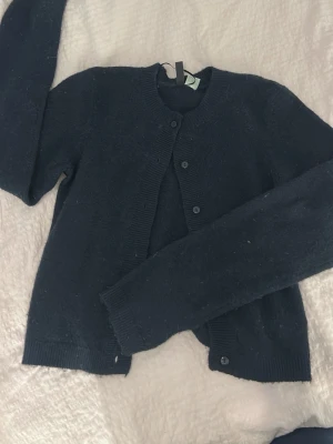 Mörkblå kofta med knappar - Mysig mörkblå kofta med långa ärmar och ribbade muddar. Klassisk rund halsringning och knäppning framtill med matchande knappar. Perfekt att slänga över en t-shirt eller linne för extra värme.