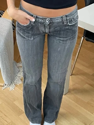 Gråa lågmidjade jeans - Säljer ett par gråa jeans med låg midja och raka ben. Jeansen har klassiska fickor både fram och bak samt tydliga sömmar och logga på bakfickan. Perfekta för dig som gillar en avslappnad och cool stil. Lappen i bak är sönder