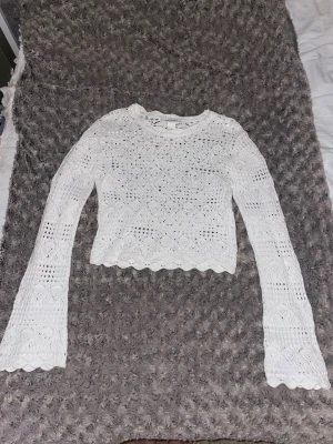 Vit stickad croppad tröja Monki XS - Säljer en vit stickad tröja från Monki i storlek XS. Tröjan är croppad med långärmade, lätt utsvängda ärmar och har ett snyggt hålmönster med geometriska detaljer. Rund hals och vågig kant nedtill ger en extra touch.