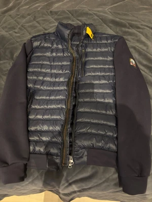  Parajumper Cardigan  - Snygg mörkblå pufferjacka från Parajumpers med quiltad kropp och släta ärmar. Jackan har dragkedja framtill, gul detalj vid kragen och klassisk PJS-logga på ärmen. Perfekt för dig som vill ha en lätt men varm jacka med sportig vibe. Har använt den 1 gång .