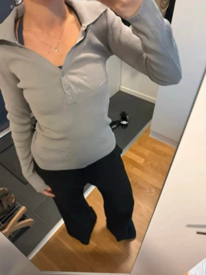 Beige ribbad långärmad topp Weekday - Säljer en beige/grå ribbad långärmad topp från Weekday i storlek S. Toppen har en djup v-ringning med tre knappar framtill och en bred krage som ger en cool retrovibe. Materialet är stretchigt och mjukt, perfekt till jeans eller kjol.