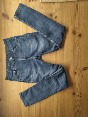 Blå skinny jeans från &Denim, strl 158 - Säljer ett par blå skinny fit jeans från &Denim i storlek 158. Jeansen har klassisk femficksdesign, gul kontrastsöm och är tillverkade i stretchigt denim-material. Passformen är tight och benen är smala hela vägen ner.