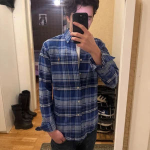 Polo Ralph Lauren skjorta  - Snygg blårutig skjorta från Ralph Lauren i slim fit. Skjortan har klassisk krage, knappar framtill och det ikoniska broderade Polo-logot på bröstet. Tillverkad i mjuk bomull som känns skön mot huden. 