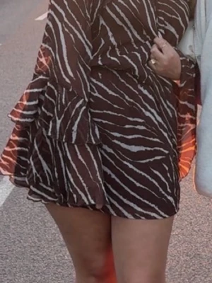 Brown Zebra Print Mini Dress – Nelly – Size M - Stylish brown zebra print mini dress from Nelly, size M. This dress features a flattering feminine fit with long sleeves, a flowy ruffle skirt, and a lightweight, slightly sheer fabric that moves beautifully.