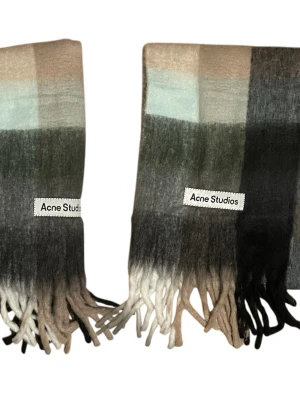 Acne Studios halsduk - Säljer en halsduk från Acne. Färgskalan går i beige, grått, svart och vitt med stora rutor och fransar nedtill. Perfekt för dig som vill ha en stilren och trendig look.