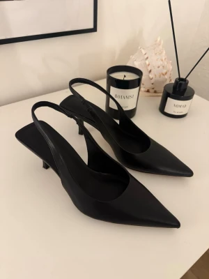 Svarta pumps med spetsig tå och låg klack - Säljer ett par stilrena svarta pumps med spetsig tå och låg klack. Skorna har öppen häl med smal rem och är tillverkade i slätt material. Bara använt en gång!