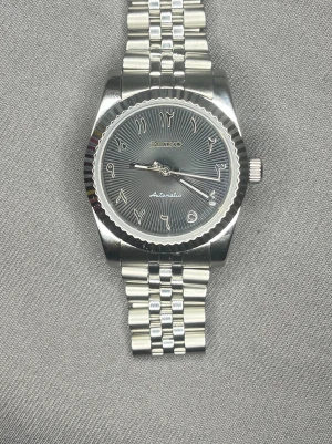 Seiko mod klocka - Bilderna visar en Seiko automatisk klocka i rostfritt stål med arabiska siffror på urtavlan och länkarmband. Ingen väst syns på bilderna. Glow in the dark