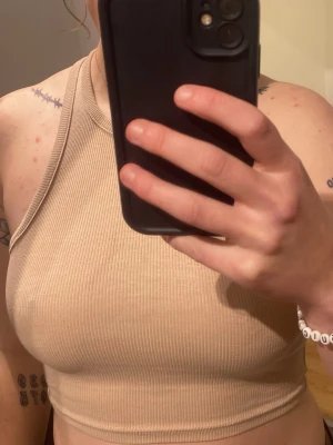 Beige ribbad linnetopp från H&M Divided - Säljer en beige ribbad linnetopp från H&M Divided i storlek XS. Toppen är croppad och har en hög halsringning med ärmlös design. Perfekt till sommaren och enkel att matcha med olika stilar.