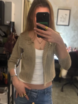 Beige stickad kofta med hålmönster - Säljer en beige stickad kofta med hålmönster och trekvartsärm. Koftan är croppad och har en luftig, öppen design som passar perfekt över ett linne eller t-shirt🥰Köpt secondhand med inget märke 