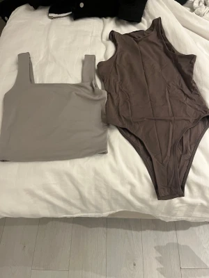 Grå topp och  bodysuit - Säljer ett set med en grå topp med breda axelband och fyrkantig urringning samt en brun bodysuit med rund hals. Båda är i mjukt, stretchigt material och har en clean, minimalistisk look. Båda två topparna säljs för 70 och en kostar 35