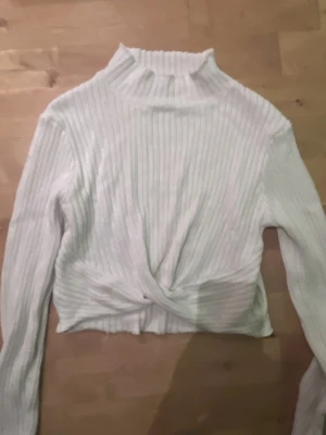 Vit ribbad croppad tröja Gina Tricot - Säljer en vit ribbad långärmad tröja från Gina Tricot. Tröjan har hög hals och en snygg twistad detalj framtill som gör den extra trendig. Croppad modell som passar perfekt till höga jeans eller kjol.