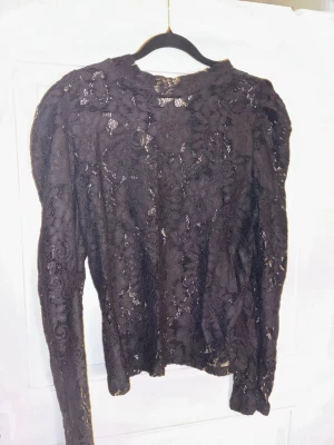 Svart långärmad topp i spets Lindex - Svart långärmad topp i spets från Lindex med blommigt mönster. Figurnära modell med lätt transparent material. I fint skick.