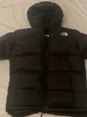 Vinterjacka Svart pufferjacka från The North Face - Säljer en svart pufferjacka från The North Face med huva och dragkedja. Jackan har en klassisk oversized look och är perfekt för kalla dagar. Loggan syns tydligt på bröstet och ryggen. Tillverkad i syntetmaterial och dun för extra värme. Ny pris 3899kr kvitto finns digitalt. Använd endast 1 vinter. Pris kan diskuteras vid snabb affär