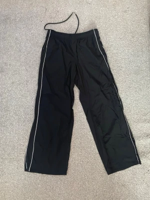 Svarta Cargo byxor  med snörning - Säljer ett par svarta cargo byxor med snörning i midjan och två vita ränder på sidan. Byxorna har en loose passform. 